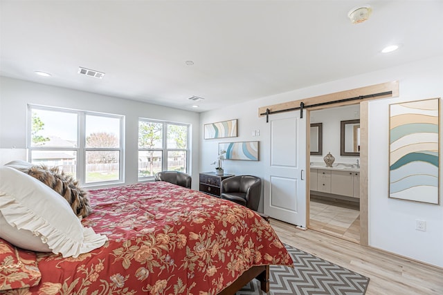 bedroom featuring a barn door, connected bathroom, and light wood-type flooring