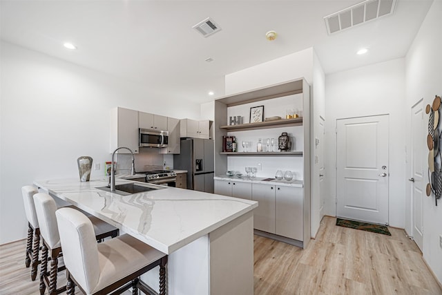 kitchen featuring gray cabinetry, a breakfast bar area, light hardwood / wood-style floors, kitchen peninsula, and stainless steel appliances