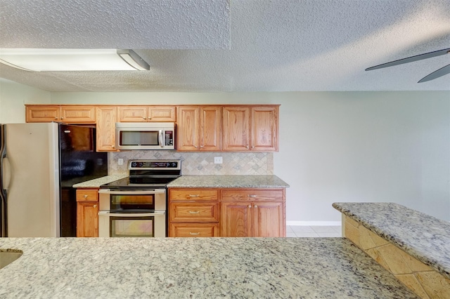 kitchen with light tile patterned flooring, appliances with stainless steel finishes, backsplash, ceiling fan, and a textured ceiling