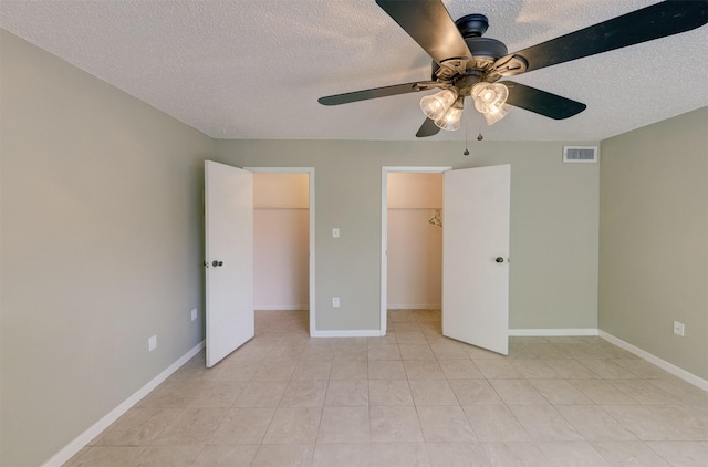 unfurnished bedroom featuring ceiling fan, a walk in closet, a textured ceiling, and a closet