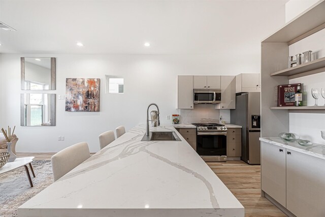 kitchen featuring light stone counters, open shelves, appliances with stainless steel finishes, light wood-style floors, and a sink