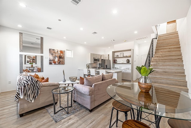 living room featuring light wood-style flooring, stairway, visible vents, and recessed lighting