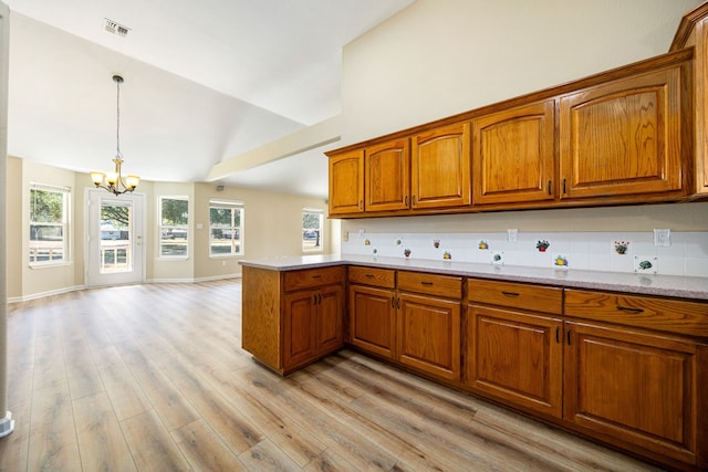 kitchen with light stone counters, vaulted ceiling, light hardwood / wood-style flooring, a notable chandelier, and pendant lighting