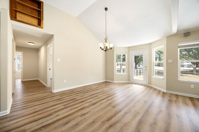 empty room featuring lofted ceiling, wood-type flooring, a notable chandelier, and plenty of natural light