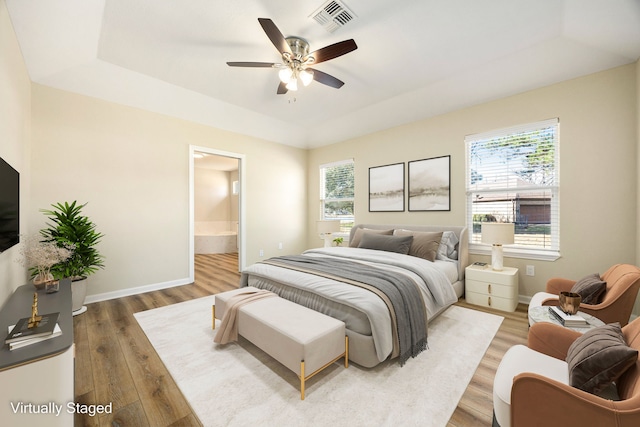 bedroom featuring ensuite bathroom, hardwood / wood-style floors, ceiling fan, and a tray ceiling