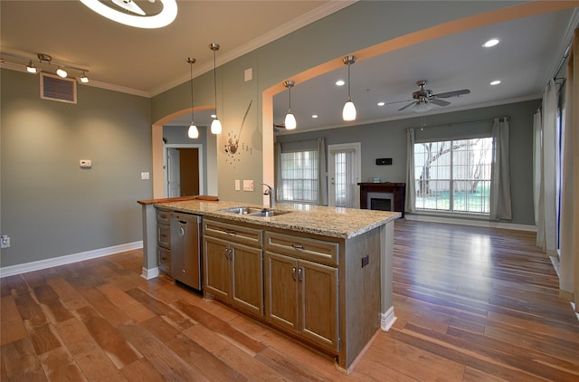 kitchen featuring sink, a kitchen island with sink, hanging light fixtures, light stone counters, and stainless steel dishwasher