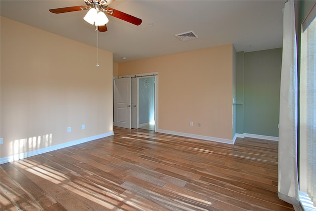 unfurnished room with hardwood / wood-style flooring, a barn door, and ceiling fan