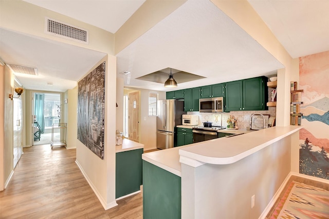 kitchen featuring green cabinetry, light wood-type flooring, appliances with stainless steel finishes, a tray ceiling, and kitchen peninsula