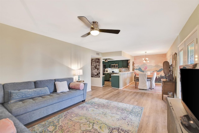 living room with ceiling fan with notable chandelier and light hardwood / wood-style flooring