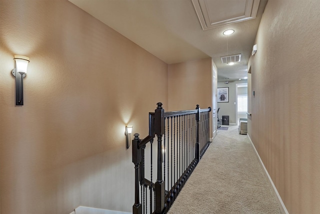 hallway with light carpet, attic access, baseboards, visible vents, and an upstairs landing