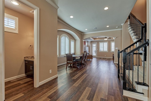 interior space featuring arched walkways, dark wood-type flooring, ornamental molding, and baseboards