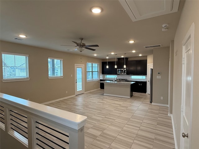 kitchen with tasteful backsplash, ceiling fan, sink, and a kitchen island with sink