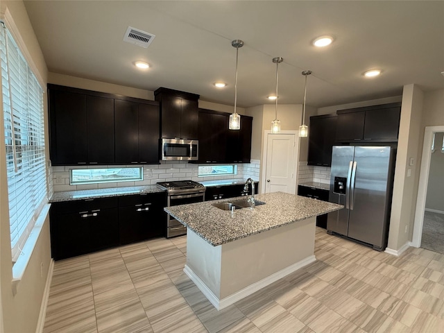 kitchen featuring sink, light stone counters, a center island with sink, pendant lighting, and stainless steel appliances