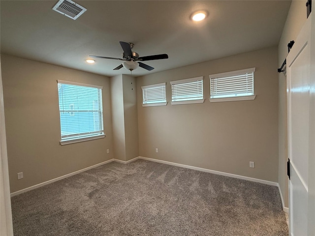 carpeted empty room with ceiling fan, a barn door, and a healthy amount of sunlight