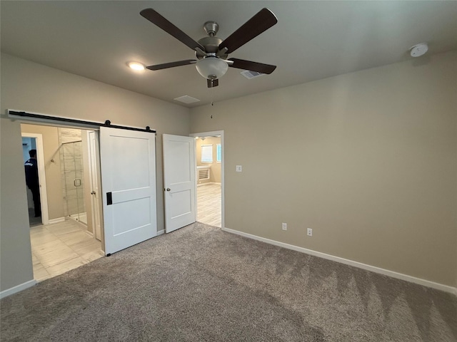 unfurnished bedroom featuring a barn door, light carpet, connected bathroom, and ceiling fan