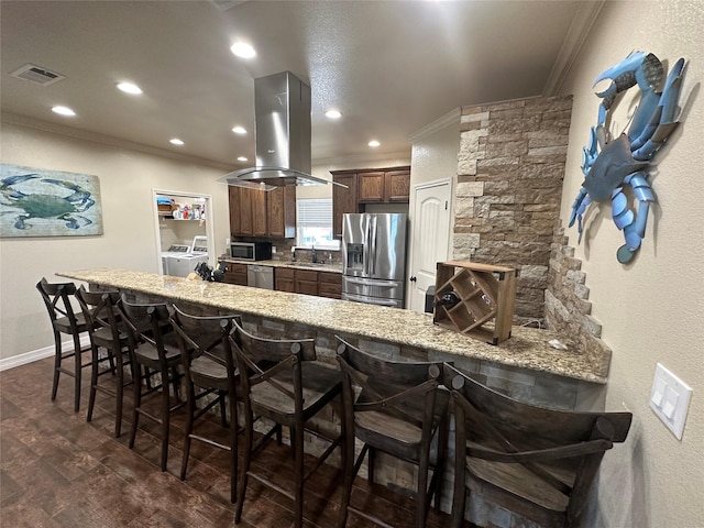 kitchen featuring a kitchen breakfast bar, kitchen peninsula, island exhaust hood, stainless steel appliances, and washing machine and dryer