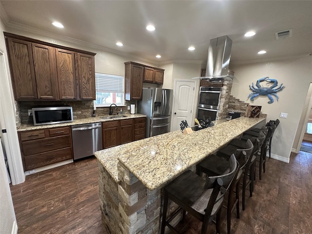 kitchen featuring a kitchen bar, kitchen peninsula, island exhaust hood, stainless steel appliances, and decorative backsplash