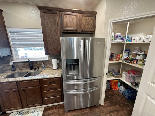 kitchen featuring stainless steel refrigerator with ice dispenser, light stone countertops, sink, and dark brown cabinetry