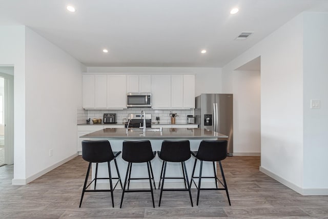 kitchen featuring tasteful backsplash, appliances with stainless steel finishes, a center island with sink, and white cabinets