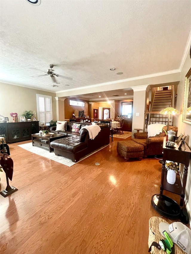 living area with a ceiling fan, a textured ceiling, ornamental molding, and wood finished floors