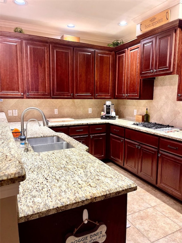 kitchen with reddish brown cabinets, a sink, light stone countertops, white gas cooktop, and backsplash