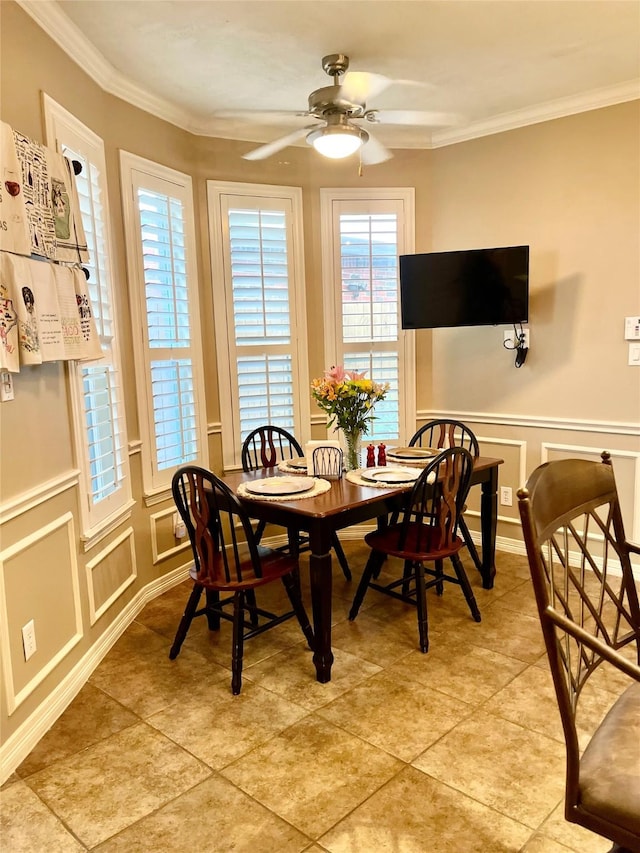 dining space with light tile patterned flooring, a decorative wall, a ceiling fan, ornamental molding, and wainscoting