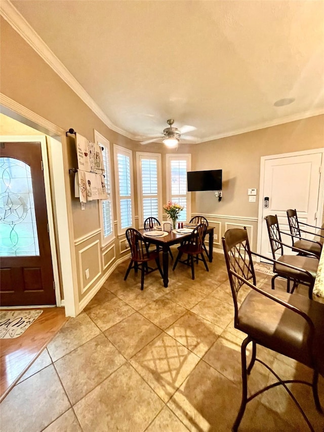 dining area featuring a wainscoted wall, ornamental molding, a ceiling fan, and a decorative wall