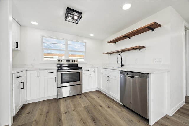 kitchen featuring wood finished floors, stainless steel appliances, white cabinetry, open shelves, and a sink