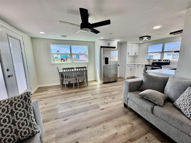 living room featuring light wood finished floors, baseboards, visible vents, and a textured ceiling