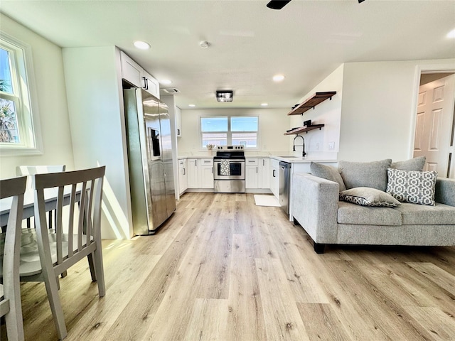 kitchen featuring appliances with stainless steel finishes, light countertops, light wood-style floors, open shelves, and a sink