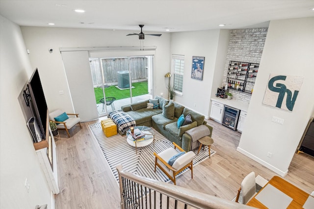 living room featuring wine cooler, ceiling fan, bar, and light wood-type flooring