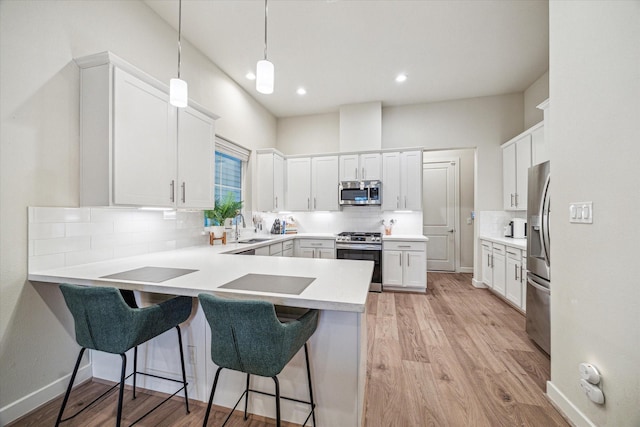 kitchen with a kitchen bar, kitchen peninsula, pendant lighting, stainless steel appliances, and white cabinets