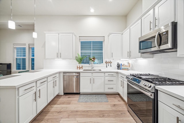 kitchen with appliances with stainless steel finishes, pendant lighting, sink, white cabinets, and kitchen peninsula