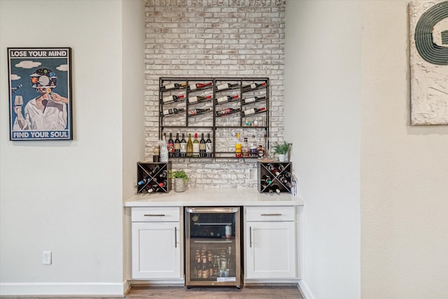 bar with white cabinets, beverage cooler, and light hardwood / wood-style flooring