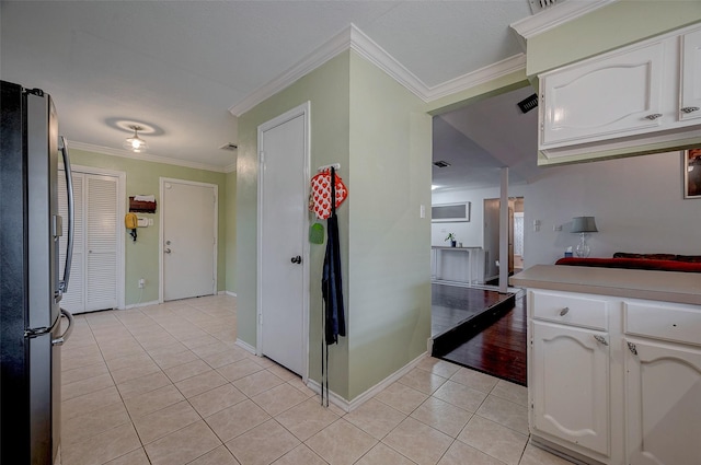 kitchen with light tile patterned floors, ornamental molding, stainless steel refrigerator, and white cabinets