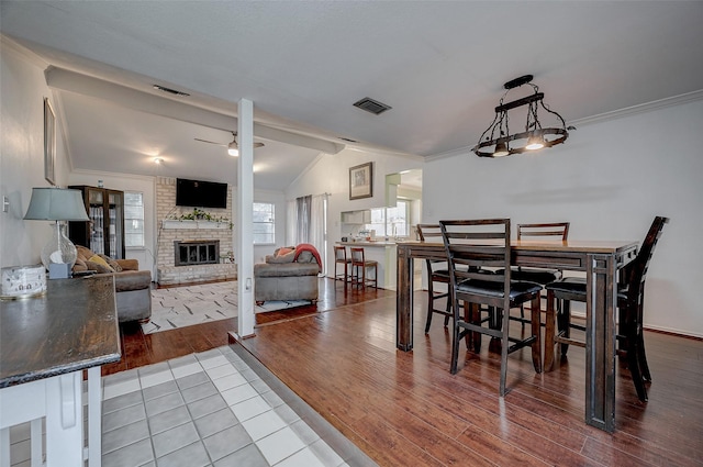 dining room featuring vaulted ceiling, hardwood / wood-style floors, a fireplace, ceiling fan, and crown molding