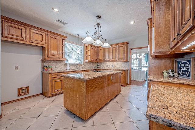 kitchen featuring pendant lighting, light tile patterned floors, a center island, a wealth of natural light, and light stone countertops