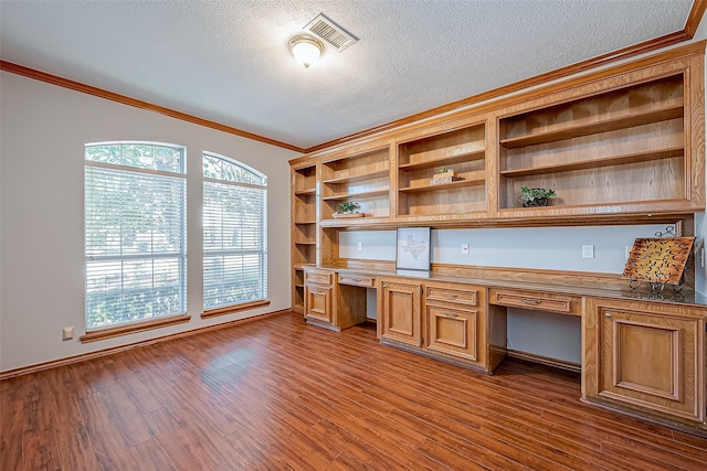 unfurnished office featuring dark hardwood / wood-style flooring, crown molding, built in desk, and a textured ceiling