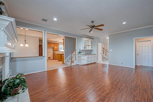 unfurnished living room with ornamental molding, ceiling fan with notable chandelier, a fireplace, and light hardwood / wood-style flooring