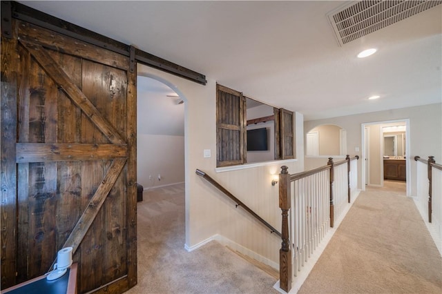 corridor featuring a barn door and light carpet