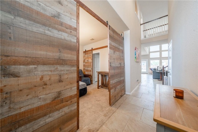 hall featuring a barn door, light carpet, and a high ceiling