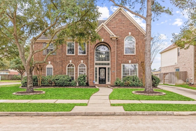 colonial-style house featuring a front yard, fence, and brick siding