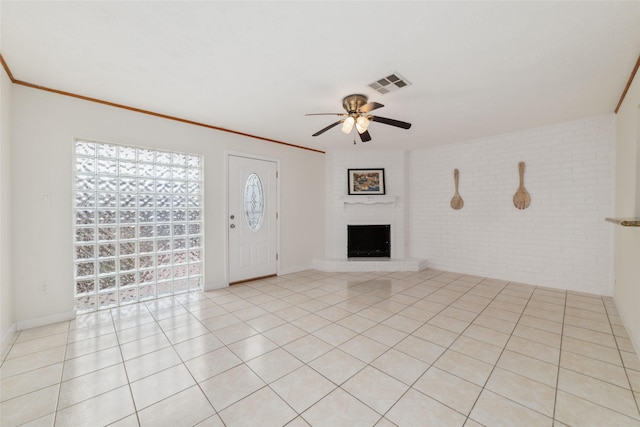 unfurnished living room with ceiling fan, brick wall, a fireplace, ornamental molding, and light tile patterned flooring