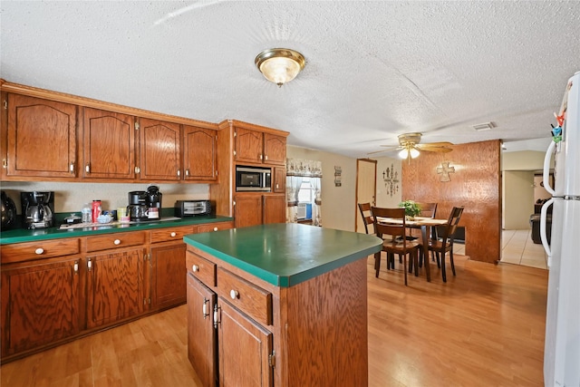 kitchen with a textured ceiling, stainless steel microwave, white fridge, a kitchen island, and light hardwood / wood-style floors