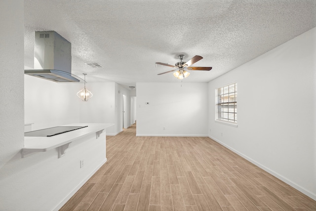 unfurnished living room with ceiling fan with notable chandelier, a textured ceiling, and light wood-type flooring