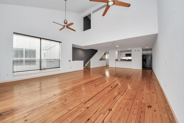 unfurnished living room featuring ceiling fan, beam ceiling, high vaulted ceiling, and light hardwood / wood-style flooring