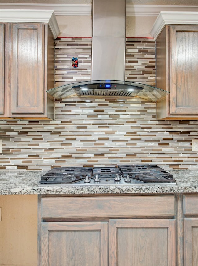 kitchen with wall chimney exhaust hood, stainless steel gas cooktop, light stone counters, crown molding, and decorative backsplash