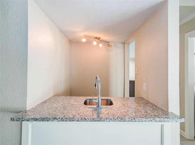 kitchen featuring sink, light stone counters, track lighting, a textured ceiling, and kitchen peninsula