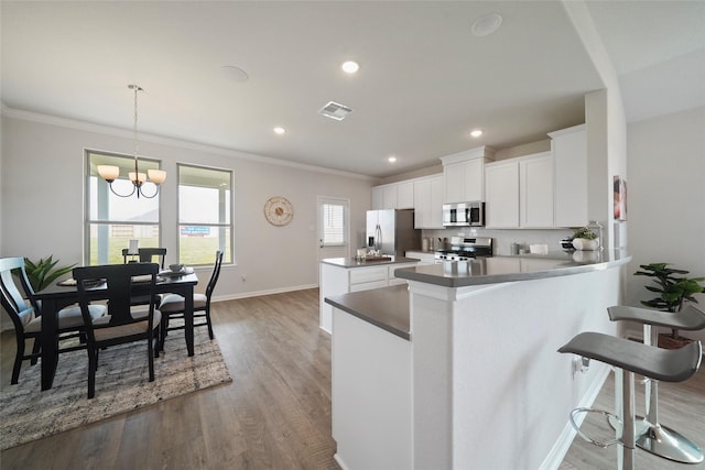 kitchen featuring white cabinetry, hanging light fixtures, hardwood / wood-style flooring, kitchen peninsula, and stainless steel appliances