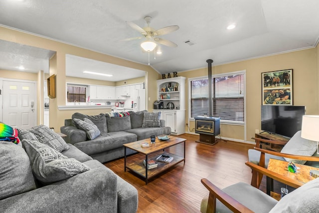 living room with crown molding, ceiling fan, dark hardwood / wood-style floors, vaulted ceiling, and a wood stove